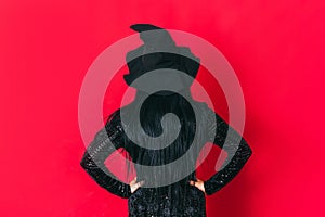 Ledy in witch costume keeps her hands on her hips facing red background