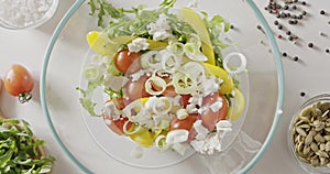 Leek fall into a glass bowl with cherry tomatoes, yellow paprika and green arugula. Background with tomatoes, pumpkin