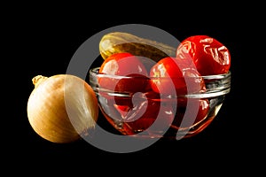 Leek and salted cucumber with tomatoes in glass vase. Onion and bowl of red tomatoes and cucumber, isolated on black background