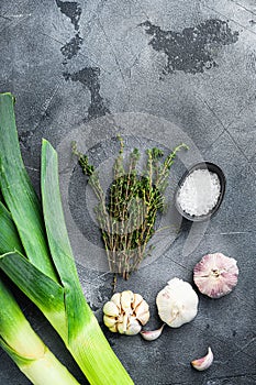 Leek stalks  with herbs ingredients for coocing Braised Leeks, on grey textured table top view