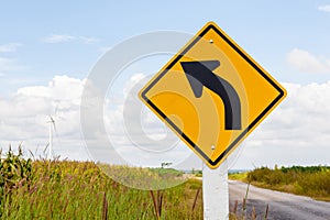 Left curved road traffic sign with windmill background and clear