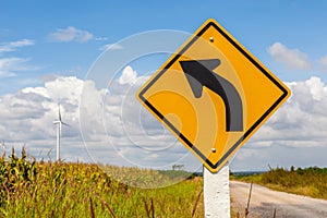 Left curved warning sign with windmill background in wind farm,