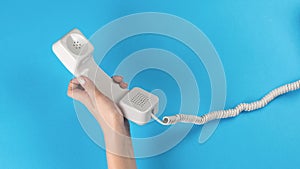 The left hand of a girl with a telephone receiver with a wire on a blue background