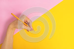 The left hand is holding a pencil and is about to write something on a bright pink-yellow background. International Left-handers