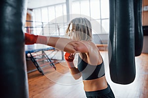 Left hand kick. Female boxer is punching the bag. Blonde have exercise in the gym