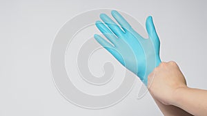 Left hand is pulling right hand wearing blue latex gloves on white background