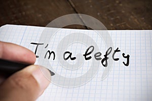 Left-handed man handwriting the text I am a lefty