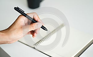 left handed man holding a pen and writing in a notebook on the table