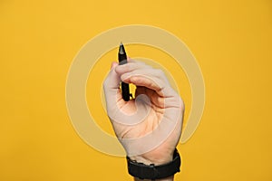 Left-handed man holding pen on yellow background, closeup