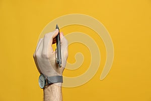 Left-handed man holding pen on yellow background, closeup. Space for text