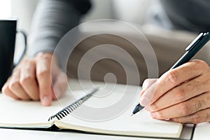Left handed man writes in a notebook on the table
