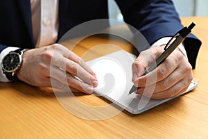 Left-handed man writing in notebook at wooden desk, closeup