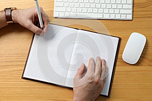 Left-handed man writing in notebook at wooden desk, top view