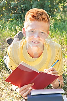 Left-handed teen lying and writing on the grass.