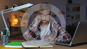 Left-handed teenage student talking on phone with fiend, preparing for test