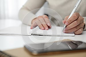 Left-handed woman writing in notebook at table indoors, closeup