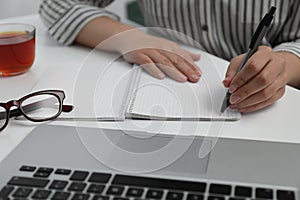 Left-handed woman writing in notebook at table indoors, closeup