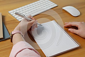 Left-handed woman writing in notebook at wooden desk, closeup