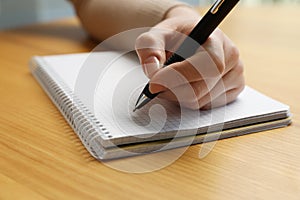 Left-handed woman writing in notebook at wooden desk, closeup