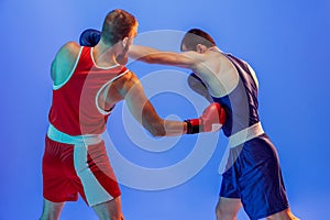 Left hook. Male professional boxers in red and blue sports uniform boxing isolated on blue background in neon light