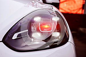 Left Led headlights of a white premium suv.  With red orange lighting from lens. New generation of car light. Closeup of a hood