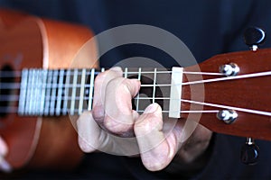 Left musician hand clamps the chord on the ukulele fretboard