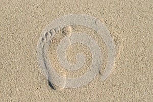 Left and right human footprints in light, yellow sand.