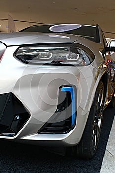 Left side detail of front mask and headlights of battery electric compact luxury crossover SUV BMW iX3. silver metallic colour