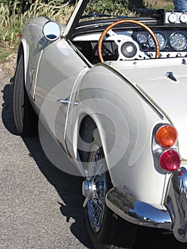 Left side of an old british classic car . Particular view of left tail light, dashboard and shiny chrome bumper . The car is a Tri