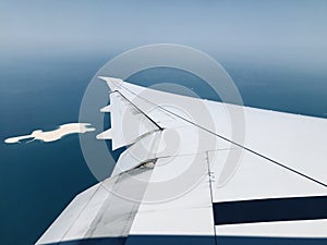 Left wings of a large flying aircraft around a ocean area