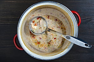 Leftovers cream fish soup in a saucepan with a ladle on a wooden table, closeup, top view