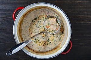 Leftovers cream fish soup in a saucepan with a ladle on a wooden table, closeup, top view