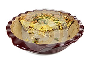 Leftovers of an egg and green onion quiche in a red ceramic baking dish