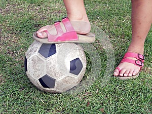 Leg of Asian little girl wear pink sandal stand on soccer ball on green grass field