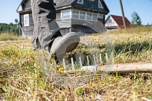 Leg of a careless, inattentive man steps on a rake, which can lead to injury, against the backdrop of a village house