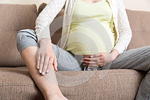 Leg cramps during pregnancy. Closeup of hands massaging swollen foot while sitting on sofa