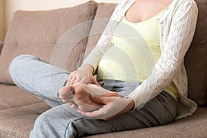 Leg cramps during pregnancy. Closeup of hands massaging swollen foot while sitting on sofa