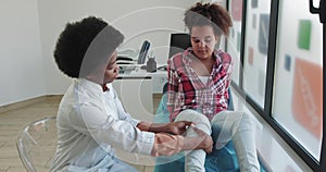 Leg dislocation first aid. doctor examines knee of African American girl. Fracture of leg in child admission to hospital