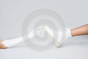 Leg of a girl in white leather boots on a light background. woman`s hand reaching for the shoe fashion photography