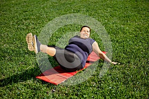 Leg lift exercise performed by body positive obese woman on lawn.