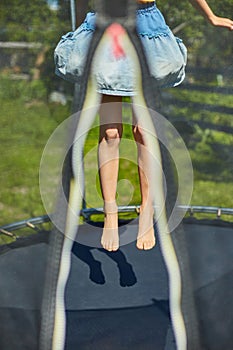 Leg of little child jumping on trampoline in the backyard of the house on a sunny summer day