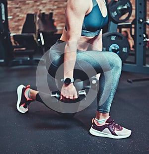 Leg muscle training, lunges with dumbbells. Athletic model woman with sports body exercising with dumbbells in the gym.