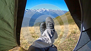 leg tourist in boots out of the tent with mountains in the background