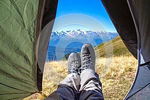 leg tourist in boots out of the tent with mountains in the background