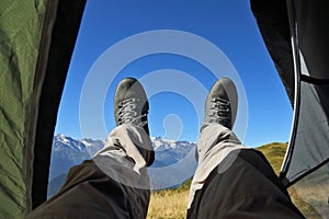 Leg tourist in boots out of the tent with mountains