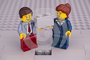 Lego businessman and businesswoman minifigures with brick ready to finishing gray building wall