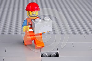 Lego worker minifigure with gray brick finishing building wall