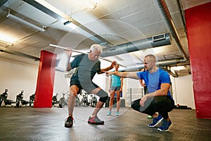 Legs apart...a senior man doing pvc pipe exercises with the assistance of his trainer.