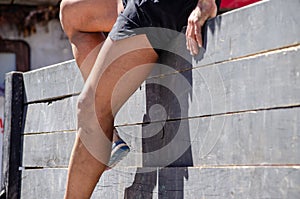 legs of an athlete participating in an obstacle course descending a vertical wooden obstacle, ocr race