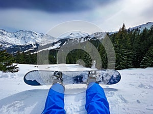 Legs attached to snowboard of as man sit in snow over ski lift